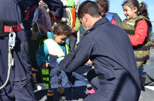 Un guardia pone un chaleco salvavidas a un niño muy pequeño que sigue muy atento lo que hace el guardia