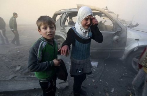 Una niña, acompañada de un niño, llora tras la explosión de una bomba de barril