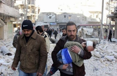 Dos hombres con aspecto desolados con la cabeza o por la calle llena de cascotes, uno de ellos lleva a un bebé en brazos con la cabeza vendada. 