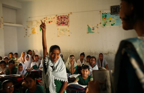 Una niña levanta la mano para llamar la atención de la profesora 