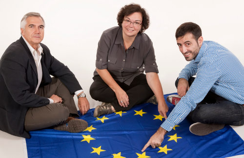 Carlos Navarro, Guillermo Bontoux y Nuria Sans sentados en el suelo sobre una bandera de Europa
