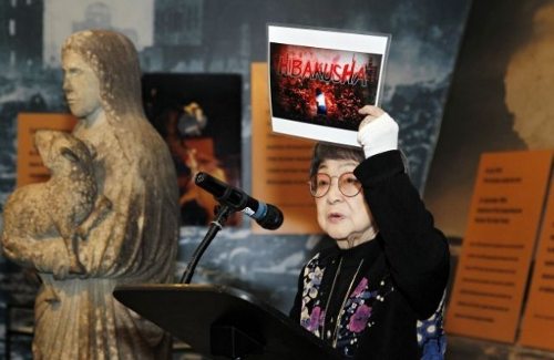 Una mujer en el podio muestra un cartel de Hibakusha