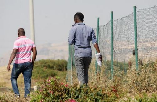 Dos inmigrantes caminan junto a una valla metálica